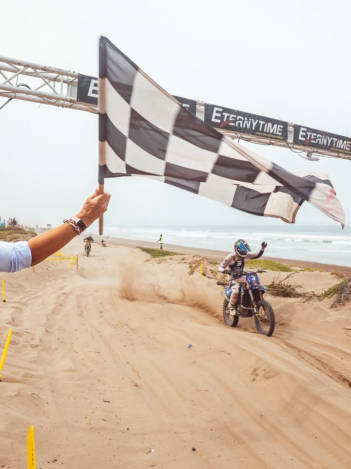 Passage d’un pilote sous le drapeau à damier et le portique ETERNYTIME lors d’une course moto sur sable