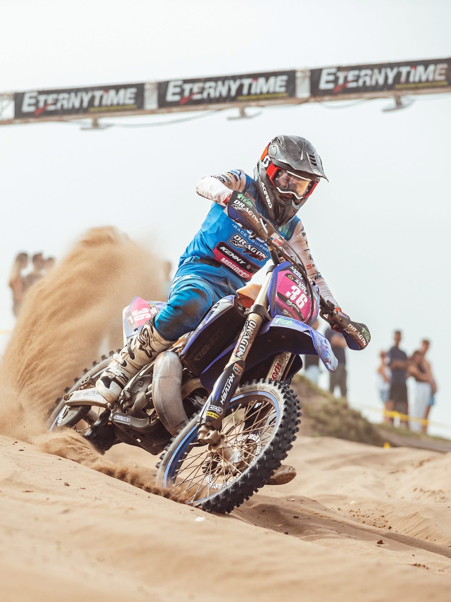 Pilote de moto en action sur le sable devant un portique ETERNYTIME